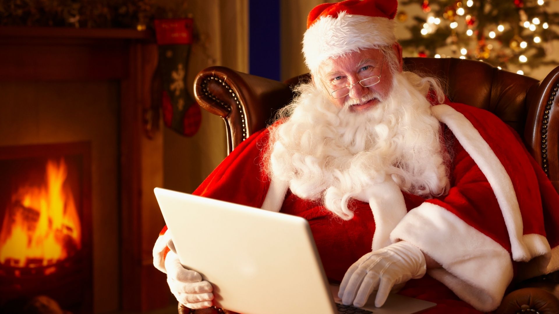 Santa sitting in front of fire, on his laptop.