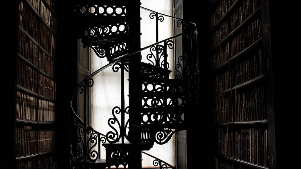Ornate spiraled staircase in a dark library.