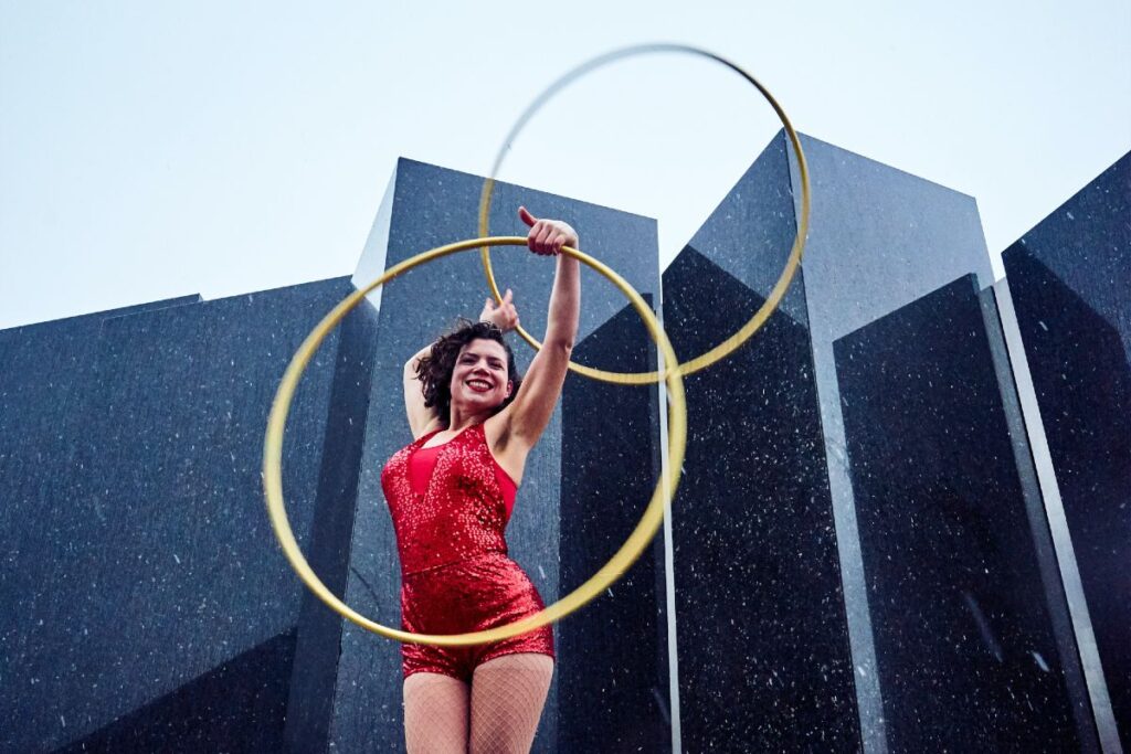 Woman in red leotard holding two hula hoops aloft.